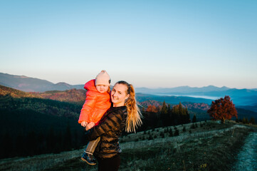 Happy family: mom hug daughter, enjoying time together, stand on sunset on top of foggy mountain. Tourists traveler on background view mockup. Hikers looking sunlight in trip in country Europe.
