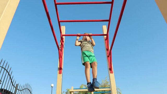 Child on pull-up bar at sports ground outdoor