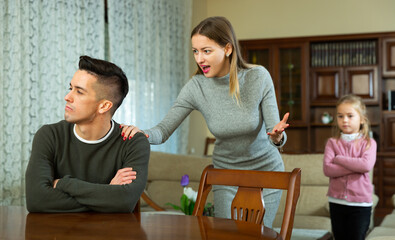 Frustrated young man sitting at home while irritated wife angrily rebuking him. Family conflicts concept