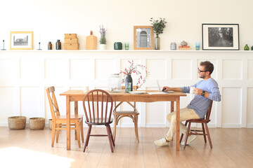 Young man with a cup of coffee works at the table at home in the morning