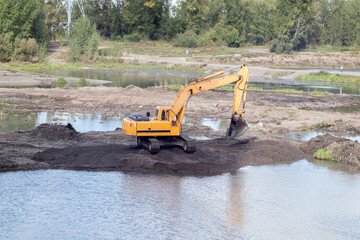 Orange Excavator working near the river dredging gravel from the river doing embankment