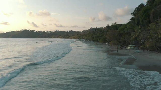 Drone aerial flying over the beach during summer holiday with people playing with the waves