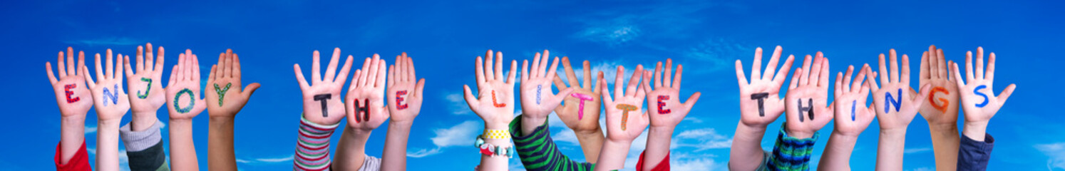 Children Hands Building Colorful English Quote Enjoy The Little Things. Blue Sky As Background