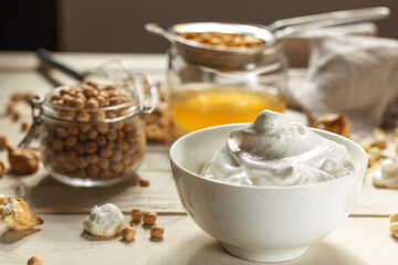 whipped soft meringue is akwafaba closeup and chickpeas in a glass jar. On a light wooden table.