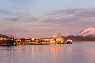 Fototapeta na wymiar The port of the town Molde in Norway in golden evening light with snow covered mountains and starting cargo airplane in background