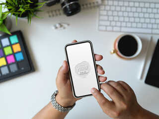Top view of man holding mock up smartphone in his office room