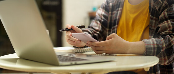 Female using smartphone while working with laptop computer