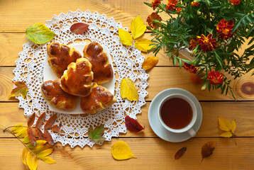 Delicious homemade breakfast with freshly baked potato pies in the form of fallen leaves on lace napkin and a cup of tea on wooden table. A vase with marigolds nearby. Beautiful autumn still life