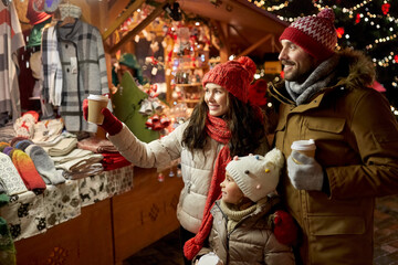 Obraz na płótnie Canvas family, winter holidays and celebration concept - happy mother, father and little daughter with takeaway drinks at christmas market on town hall square in tallinn, estonia