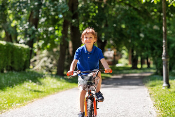 childhood, leisure and people - happy smiling little boy riding bicycle at summer park