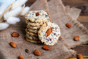 Pile of homemade almond multi grain cookies on burlap with dried almond and dried flowers on wooden table. Healthy dessert concept