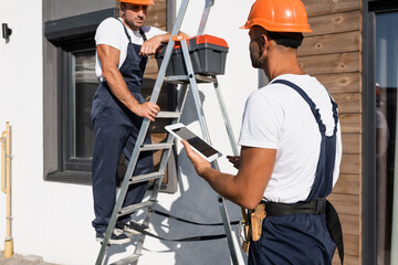 Selective focus of handyman with digital tablet standing beside colleague in uniform on ladder and house © LIGHTFIELD STUDIOS
