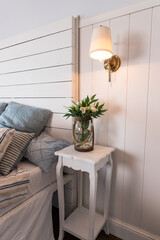 Bright and comfortable bedroom interior design in scandinavian style.Flowers on bedside table....
