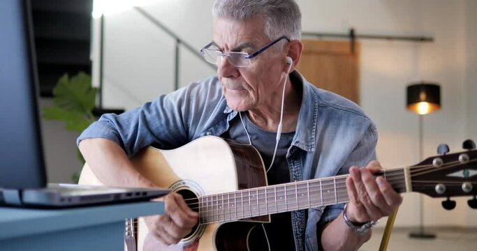 old man learning to play guitar watching tutorial on laptop,senior caucasian male practicing and playing musical instrument,hobby activity passion