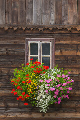 Fototapeta na wymiar Blumendekoration vor Fenster am Holzhaus