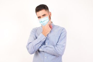 Portrait of thoughtful smiling man keeps hand under chin, looks directly at camera, listens something with interest, dressed casually, poses against gray wall. Youth concept.