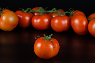 Rote frische Tomaten, vorne eine einzeln, im Hintergrund eine Rispe auf einem schwarzen Hintergrund