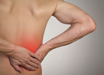 Lower back pain in a man. Highlighted in red. On a gray background. Close up
