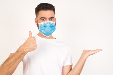 Young happy cheerful man showing thumb up and pointing with the other hand while standing indoors. Good Job. Wearing casual clothes.