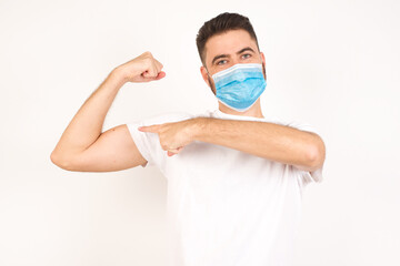 Waist up shot of blond man raises hand to show his muscles, feels confident in victory, looks strong and independent, smiles positively at camera, stands against gray background. Sport concept.