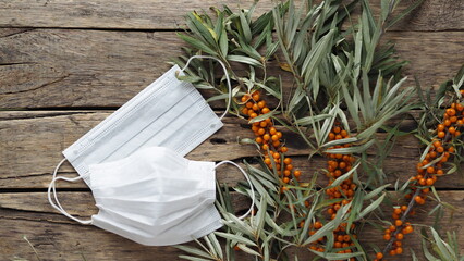 The concept of the protection and treatment of influenza with folk remedies using the beneficial sea buckthorn berries. Medical masks with sea buckthorn branches with berries on a wooden background.
