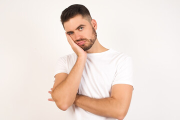 Fototapeta premium Very bored adult man with beard holding hand on cheek while support it with another crossed hand, looking tired and sick, over gray background. Father attends parents day at school
