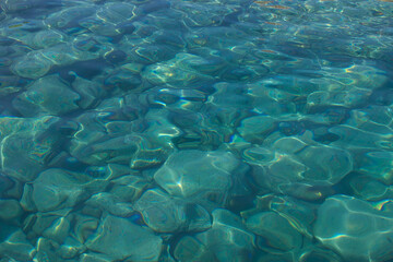 Fototapeta na wymiar Large grey rocks in clear flat turquoise blue sea water natural background