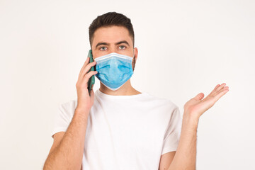 Young businessman wearing medical mask talking on the phone over white background stressed with hand on face, shocked with shame and surprise face, angry and frustrated. Fear and upset for mistake.