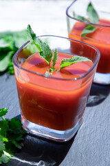 2 glasses of fresh tomato juice with mint and parsley on a black, top view. Vegan, healthy lifestyle concept