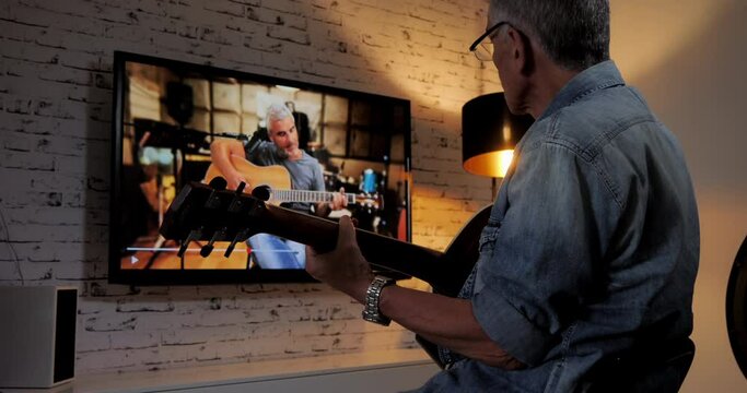 old man follow online class tutorial on internet television smart tv to learn to play guitar,person spending time on his passion hobby at home
