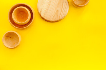 Set of rustic wooden tableware - bowls and utensils on yellow background top view