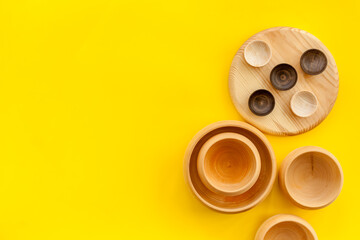 Set of rustic wooden tableware - bowls and utensils on yellow background top view