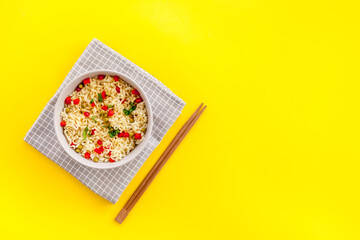 Instant noodle with pepper,peas, chopstick and tower. Yellow background top view copy space