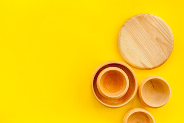 Set of rustic wooden tableware - bowls and utensils on yellow background top view