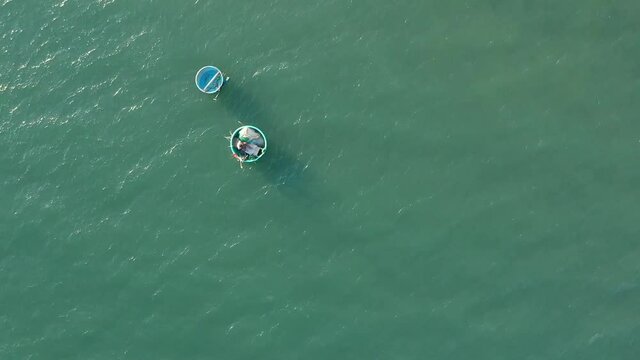 Aerial view of beautiful sea. Fisherman is seating in round boat and sorting fishing net. Man in vietnamese hat in fishing boat  in the blue water. Asian fishing ship in ocean. Sandy shore with palm