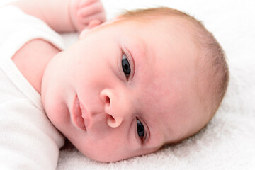 Cute newborn baby boy face close up on a white blanket