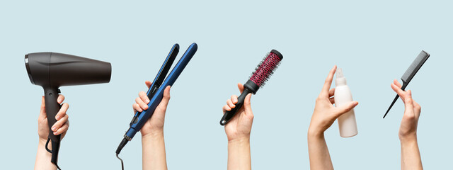 Woman hands holding hairdryer, straightener, hairbrush, tail comb and hair care essence in bottle isolated on blue background, horizontal banner format