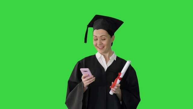 Happy female graduate holding diploma and texting on her phone on a Green Screen, Chroma Key.