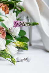 Wedding accessories. Pearl earrings with diamonds, white shoes and a bridal bouquet with white roses on a light background.