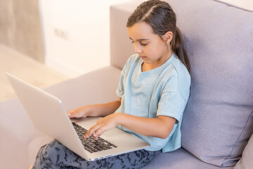 Little girl doing her homework at home and using a laptop