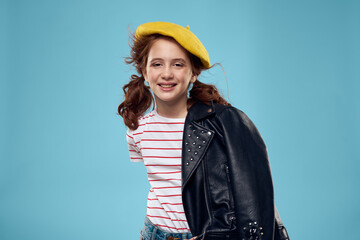 beautiful girl with a black jacket and a yellow hat on her head red hair model blue background