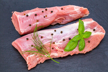 raw pork tenderloin with herbs on a black tray
