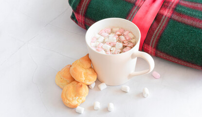 Christmas hot drinks. White cup of hot chocolate drink with marshmallows and cakes, warm plaid, Christmas balls on a white marble background. Winter time. View from above. Christmas holidays concept