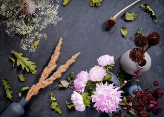 Autumn flower arrangement. A bouquet of asters is in a vase. There are various dried flowers and oak leaves nearby. Dark concrete background. Autumn concept. Birthday card. Flat lay. Top view.