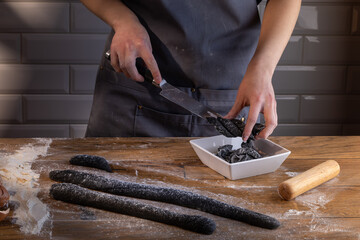 Chef preparing and cutting the dough for cooking black dumplings with sepia addition on the wooden table. Cooking dumplings – step by step guide.