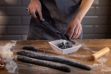 Chef preparing and cutting the dough for cooking black dumplings with sepia addition on the wooden table. Cooking dumplings – step by step guide.