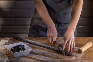 Chef preparing and cutting the dough for cooking black dumplings with sepia addition on the wooden table. Cooking dumplings – step by step guide.