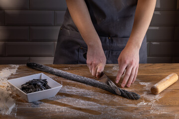 Chef preparing and cutting the dough for cooking black dumplings with sepia addition on the wooden table. Cooking dumplings – step by step guide.