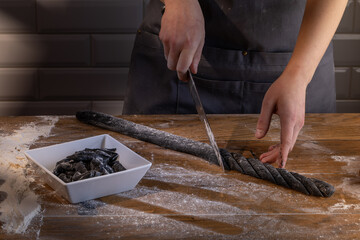 Chef preparing and cutting the dough for cooking black dumplings with sepia addition on the wooden table. Cooking dumplings – step by step guide.
