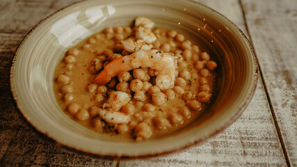 Chickpea stew with spanish prawns on wooden table in a restaurant